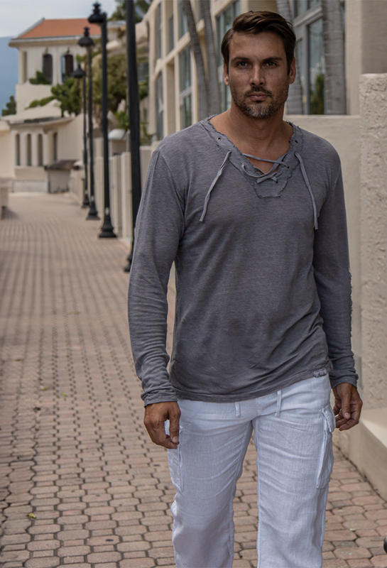 A man wearing linen clothing walking along a coastal sidewalk in Italy.