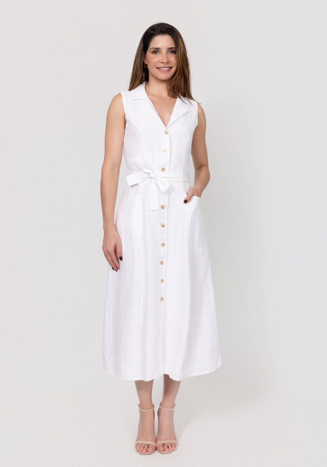Woman wearing a white sleeveless linen dress on a plain background