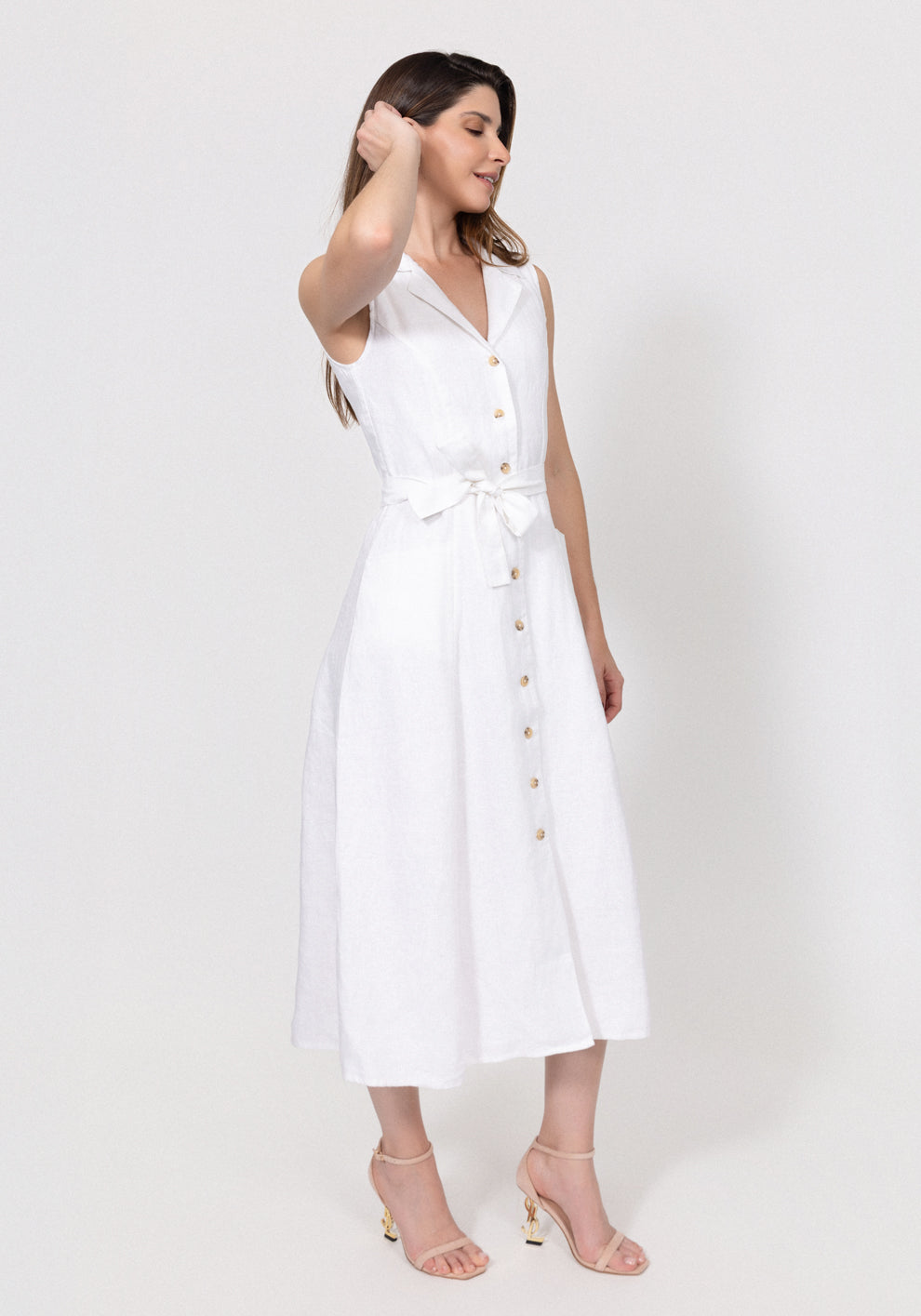 Woman wearing a white linen sleeveless dress with buttons on a white background