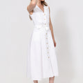 Woman wearing a white linen sleeveless dress with buttons on a white background
