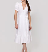 Woman wearing a white Linen Wrap Dress with Puff Sleeves and Ruffle Hems on a light gray background