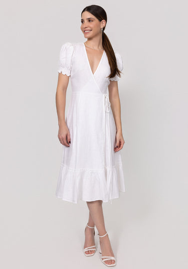 Woman wearing a white Linen Wrap Dress with Puff Sleeves and Ruffle Hems on a light gray background