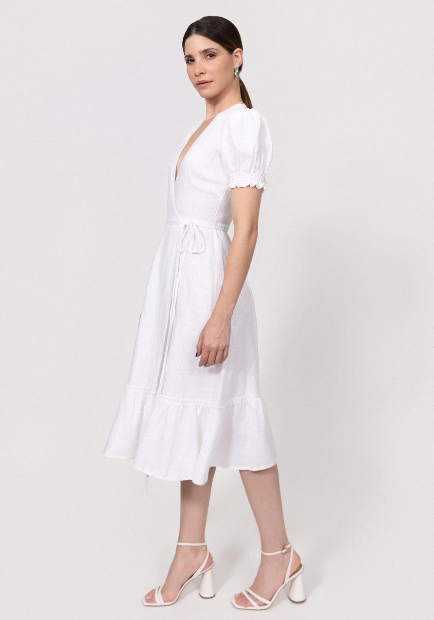 Woman wearing a white Linen Wrap Dress with Puff Sleeves and Ruffle Hem on a plain background