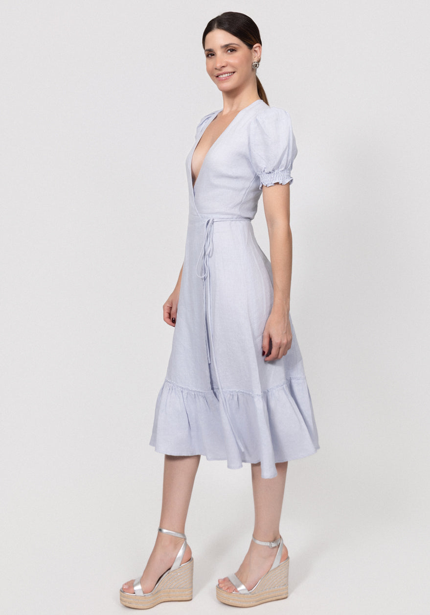 Woman wearing a light blue Linen Wrap Dress with Puff Sleeves and Ruffle Hem with a white background